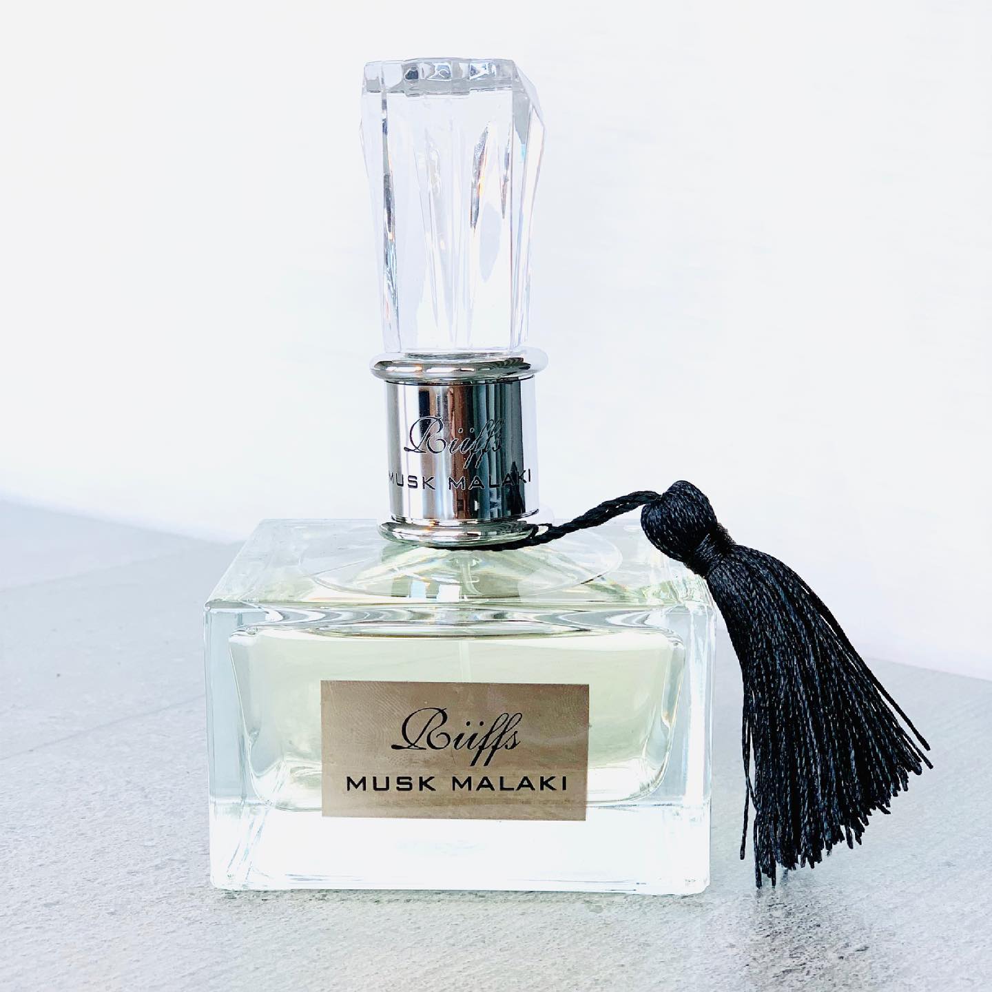 Perfume bottle labeled 'Räiffs Musk Malaki' with a black tassel on a light background