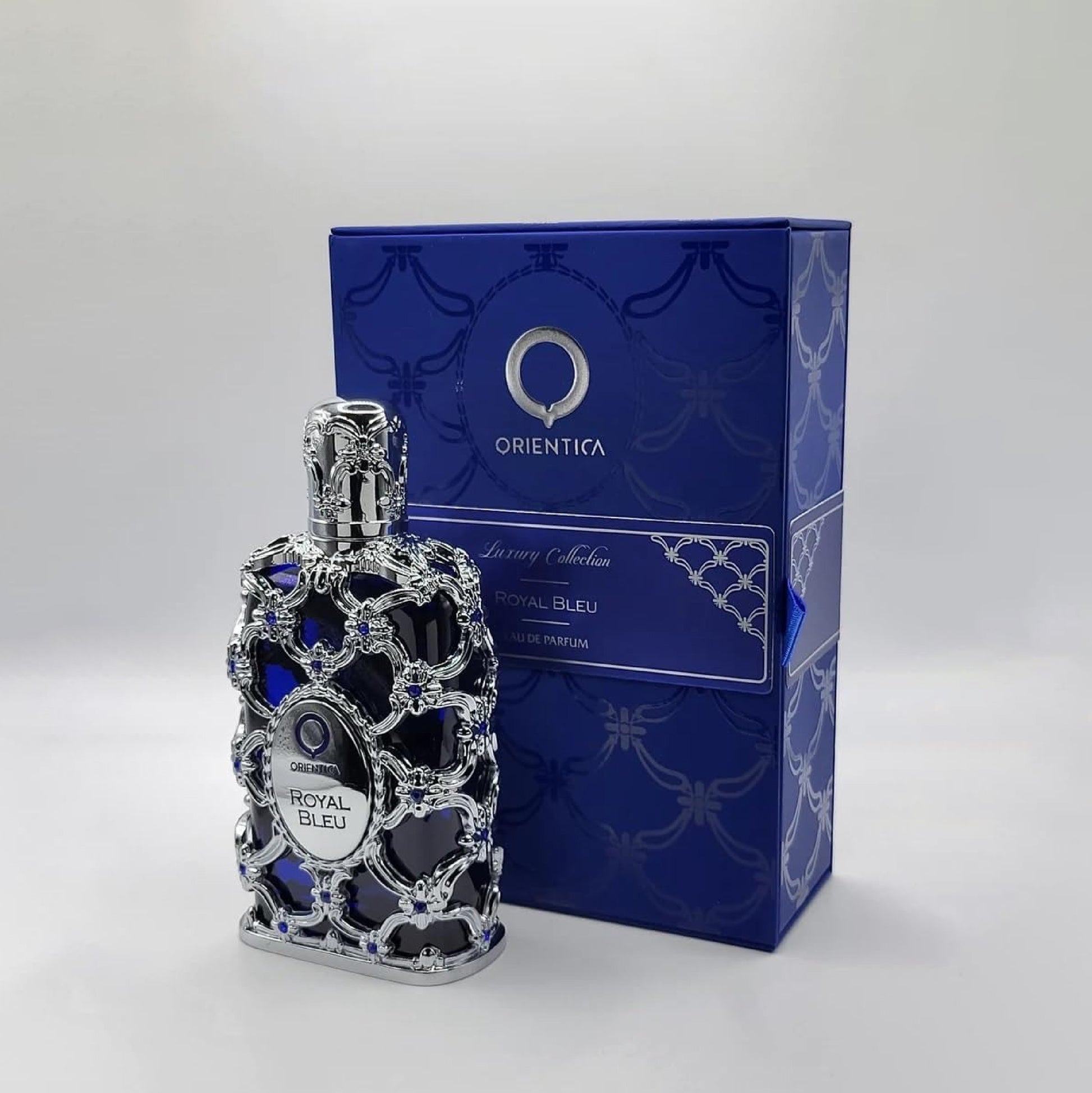 Perfume bottle with intricate design next to its packaging on a white background