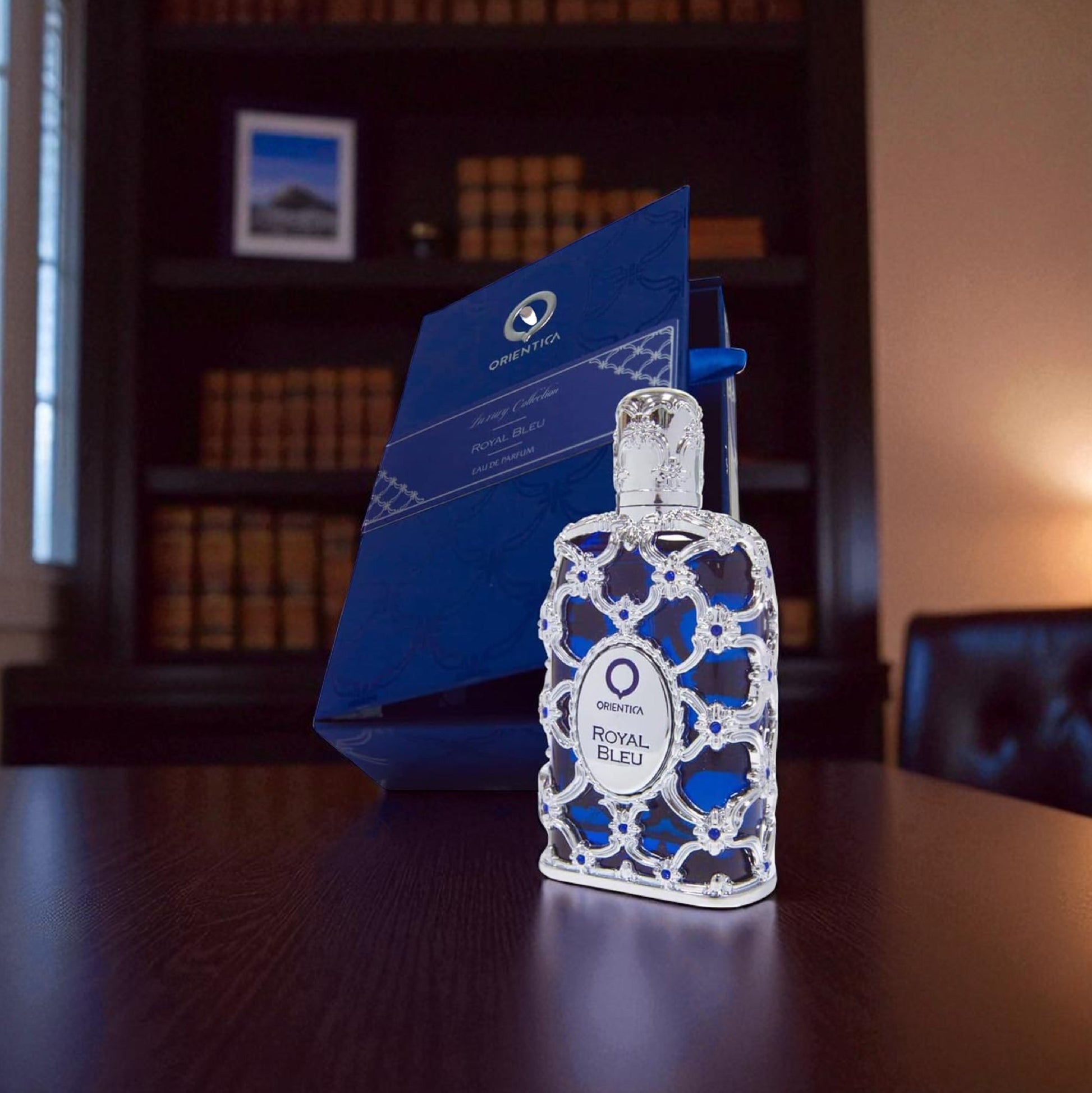 Decorative bottle with blue and white pattern on a wooden surface, with a blurred background of books and a picture frame.