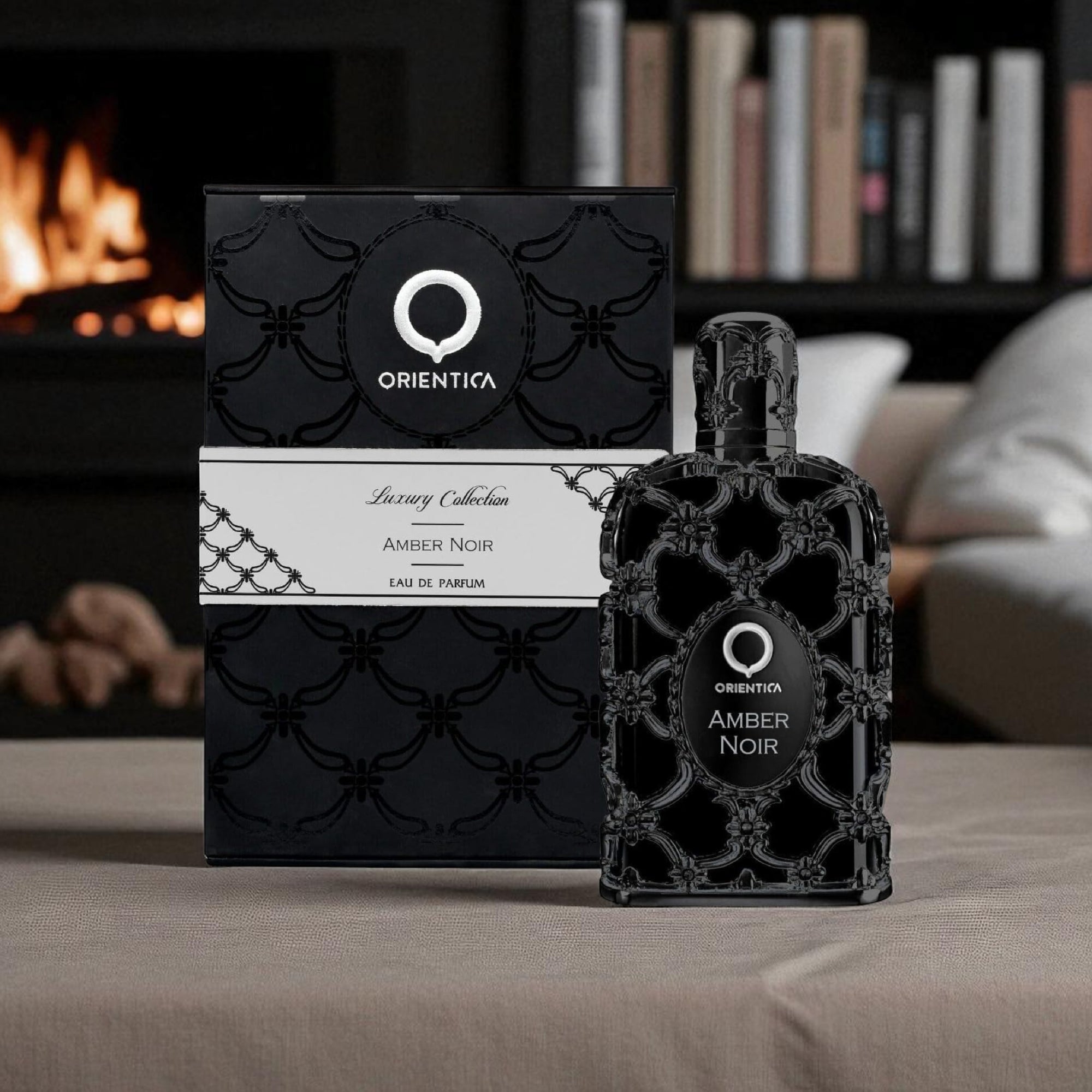 Orientalia Amber Noir perfume bottle and packaging on a table with a fireplace and books in the background