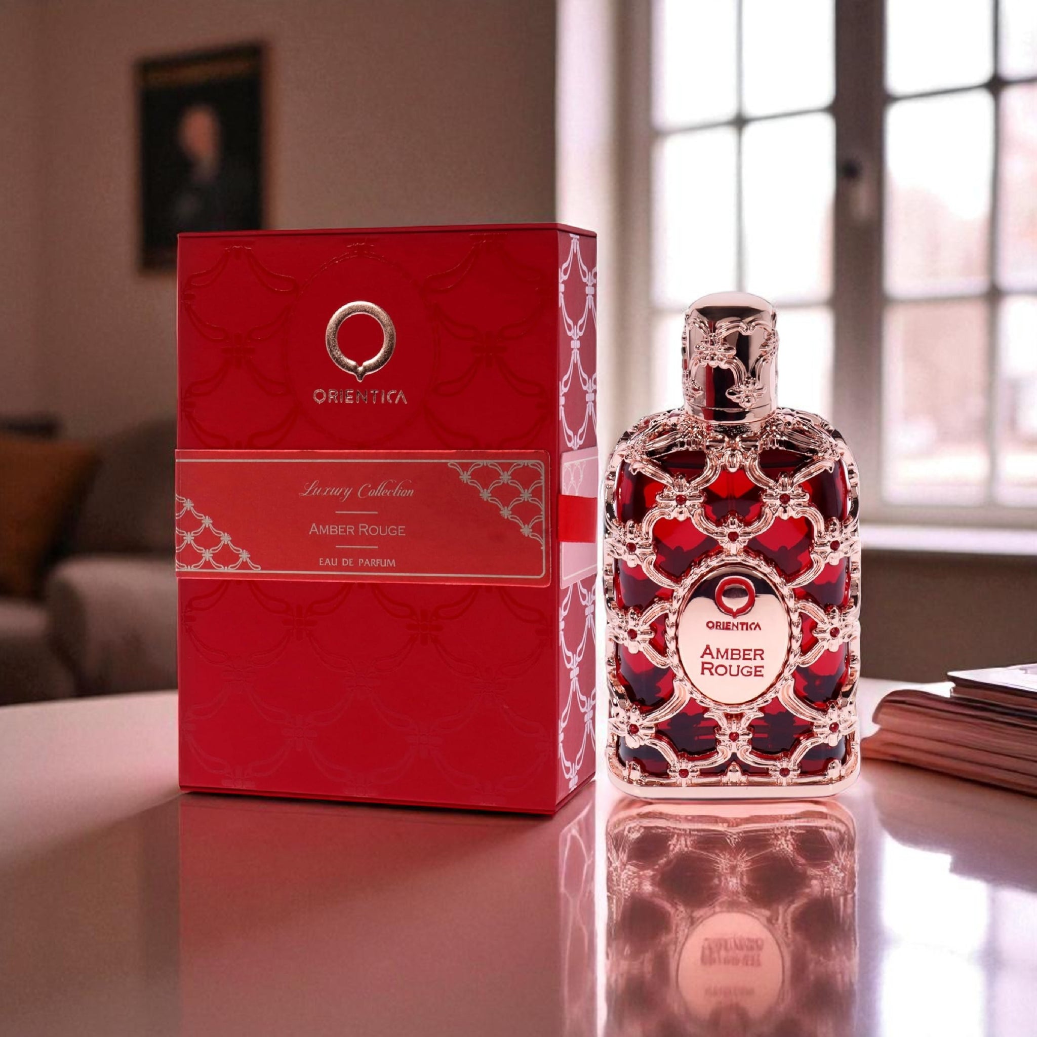 Oriental Amber Rouge perfume bottle and packaging on a reflective surface with a blurred background