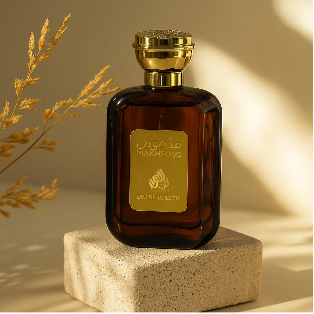 Brown perfume bottle with gold cap and label on a beige surface with dried grasses.
