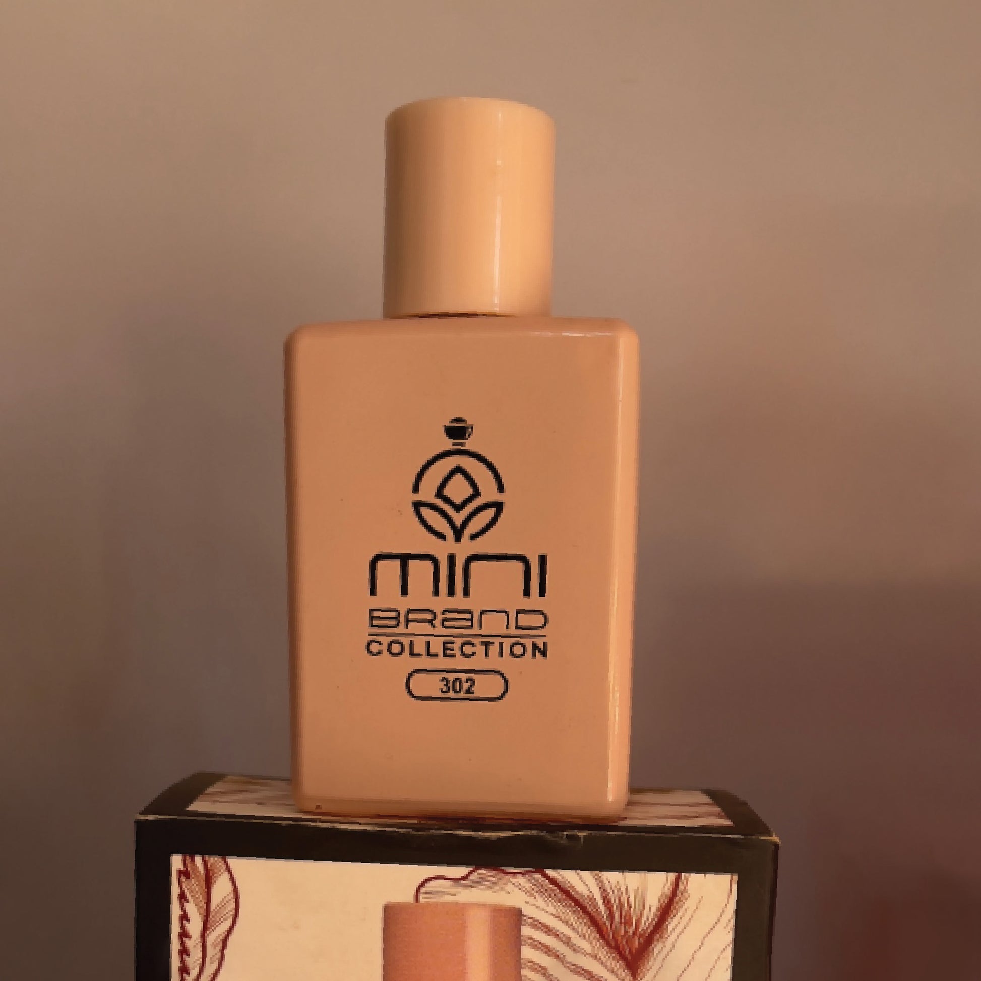 Beige perfume bottle with 'mini brand collection' logo on a wooden stand against a brown background