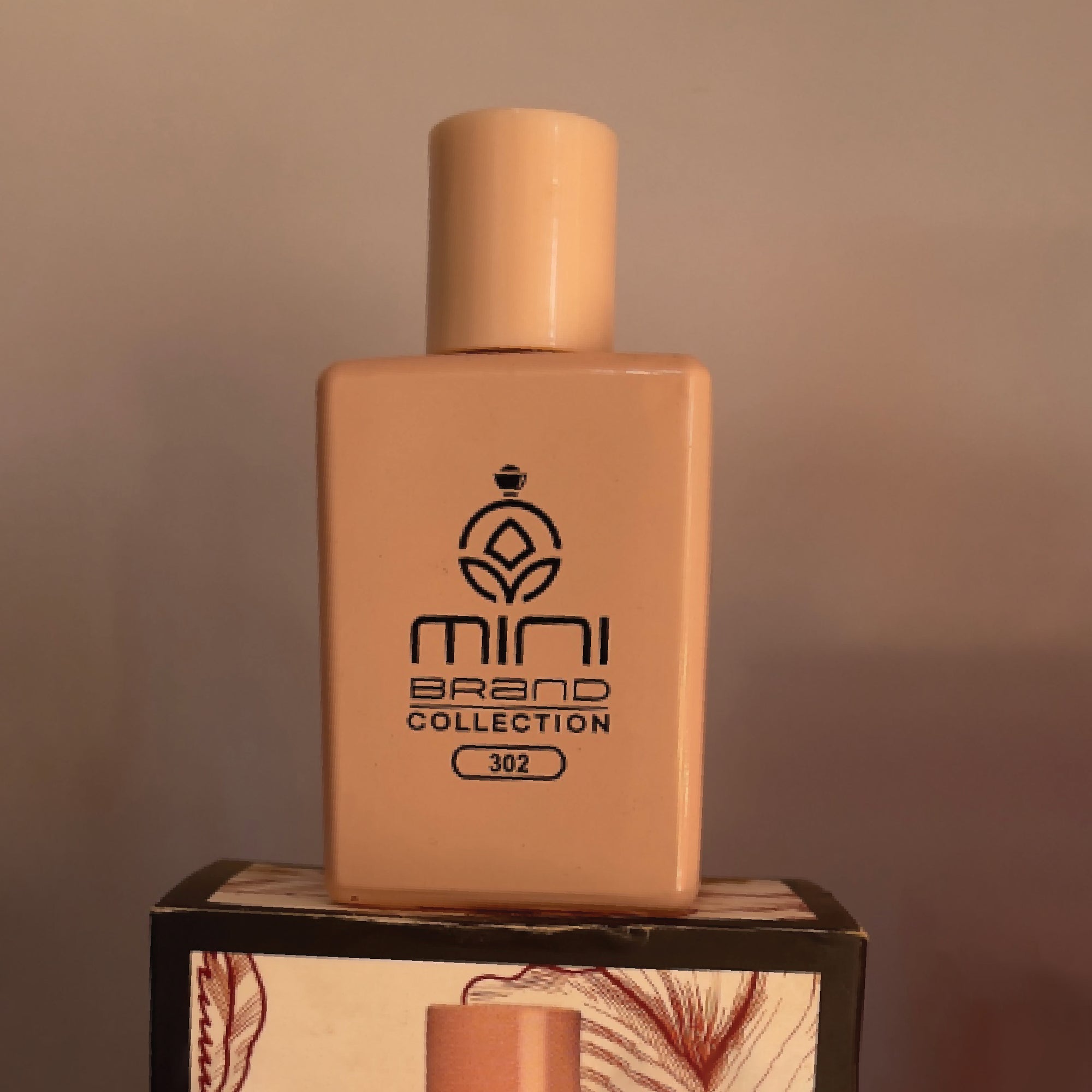 Beige perfume bottle with 'mini brand collection' logo on a wooden stand against a brown background