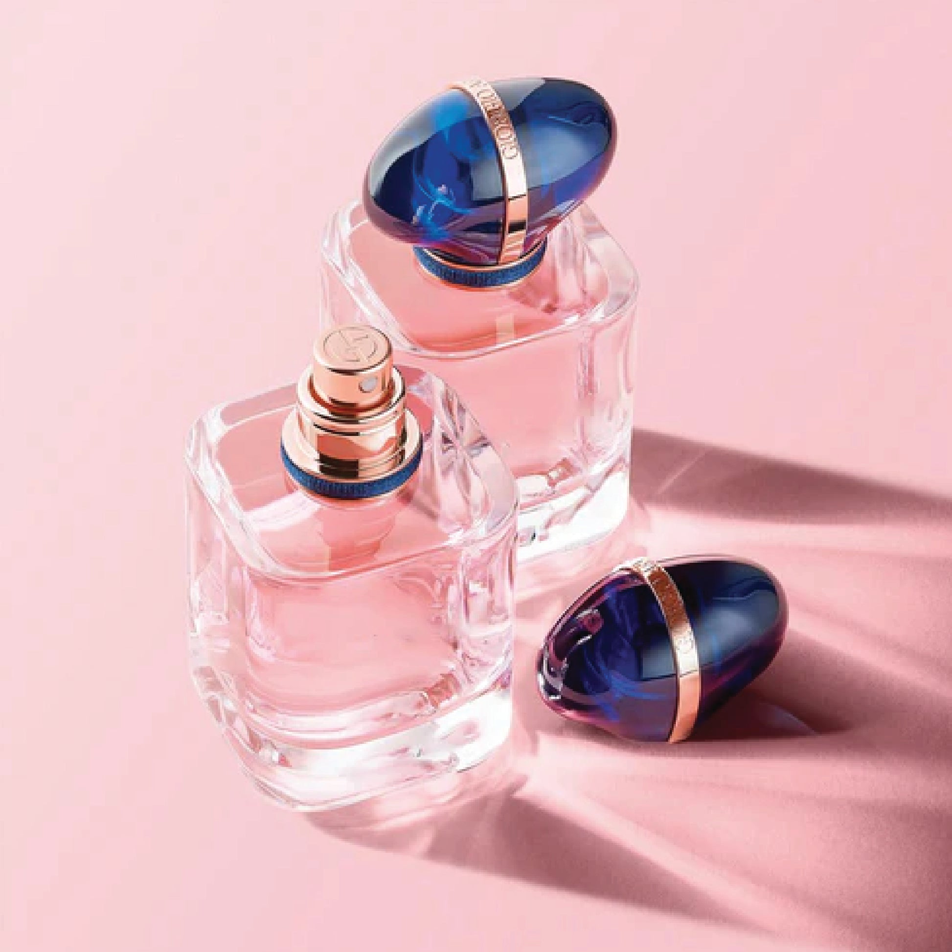 Two perfume bottles with blue caps on a pink background