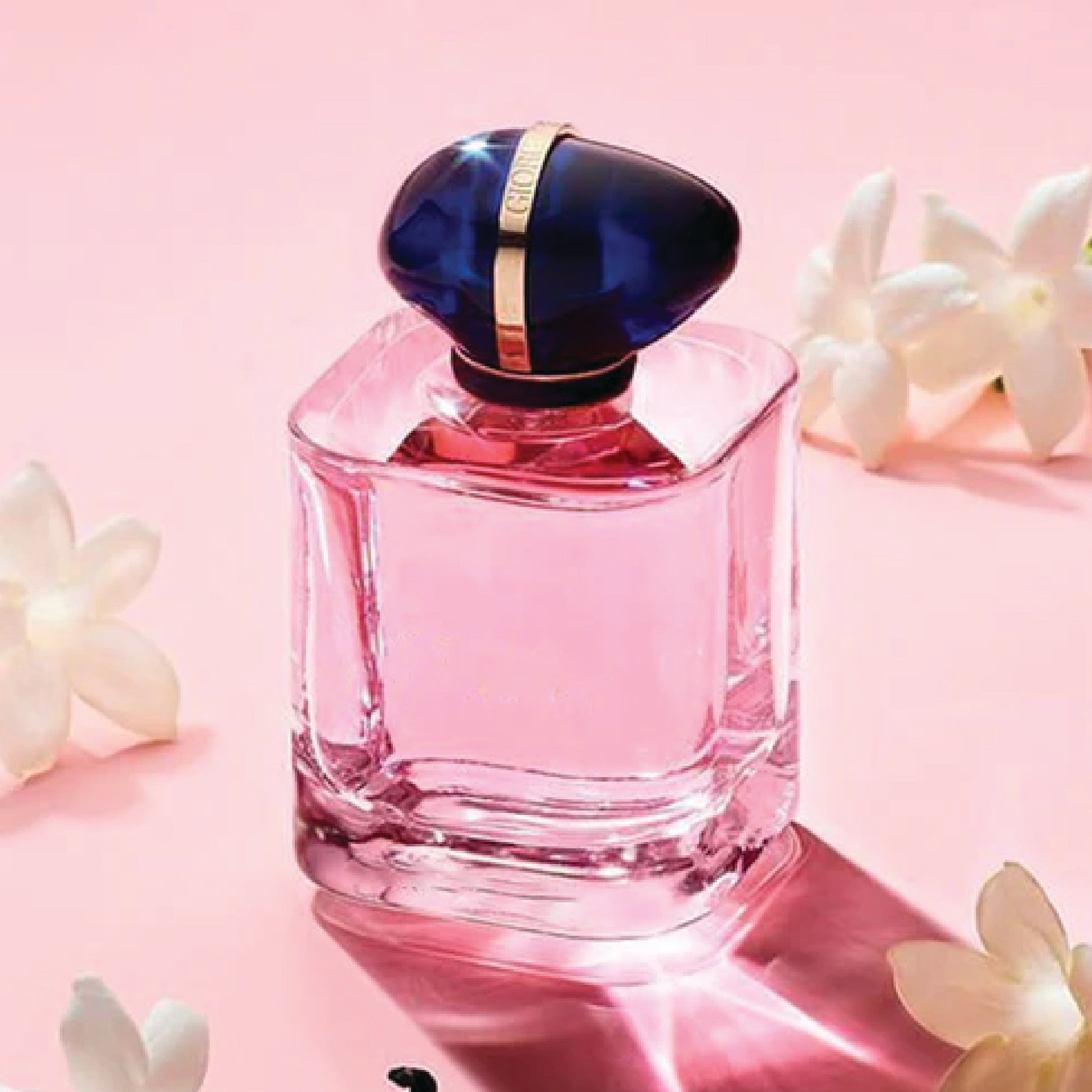 Pink perfume bottle with blue cap on a pink background with white flowers