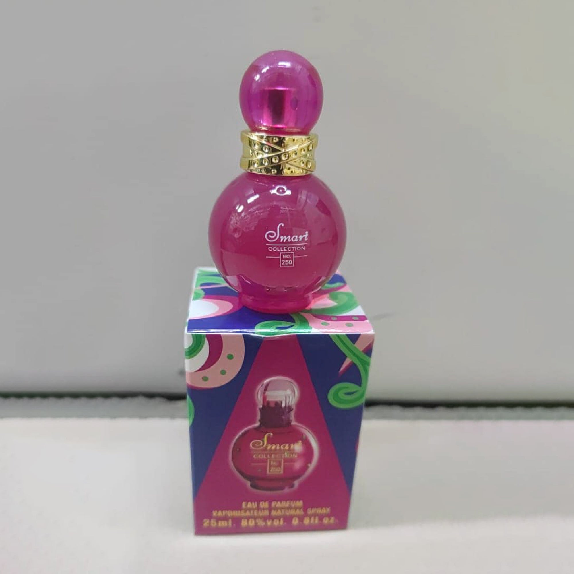 Pink perfume bottle with gold cap on a colorful box against a white background