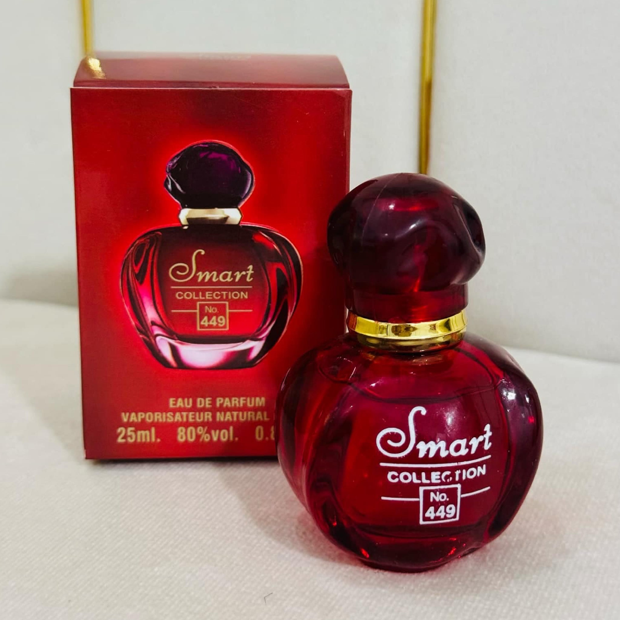 Red perfume bottle with gold cap and 'Smart Collection' branding next to its packaging on a white surface.
