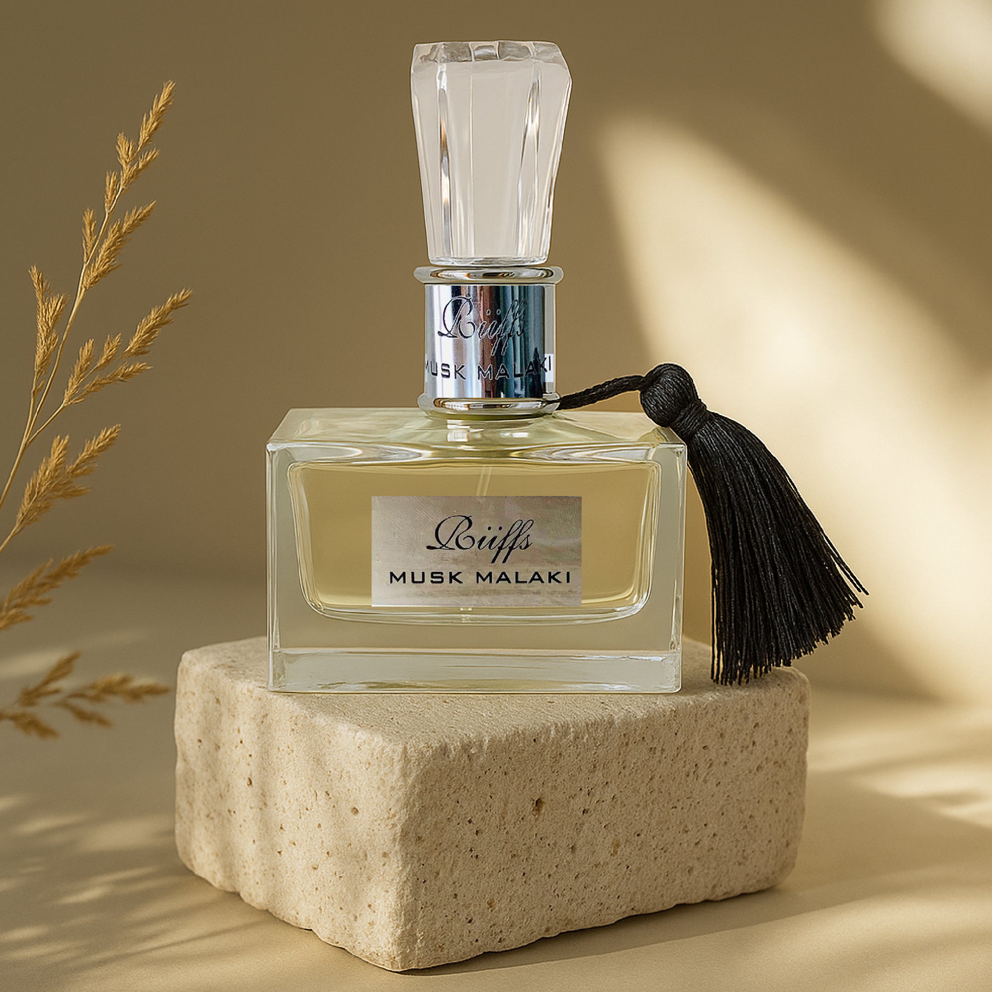 Perfume bottle labeled 'Musk Malaki' with a tassel on a beige stone block against a warm background.